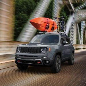 Grey Jeep Renegade driving on a bridge with a orange canoe strapped to the top. 